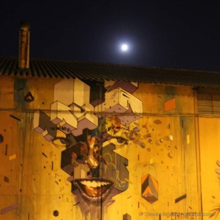 Großes Wandbild mit kubisch zerlegtem Gesicht an einer Hallenwand, darüber der Vollmond